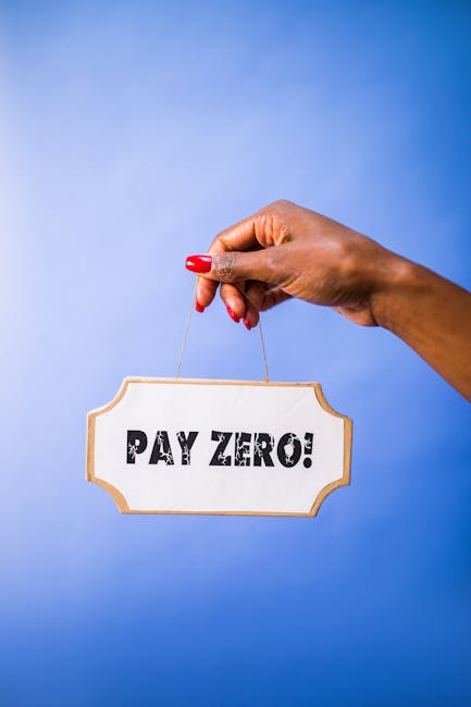 A person's hand with red painted nails is holding a small wooden sign by a string against a plain blue background. The sign has a white background with a brown border and displays the bold black text 