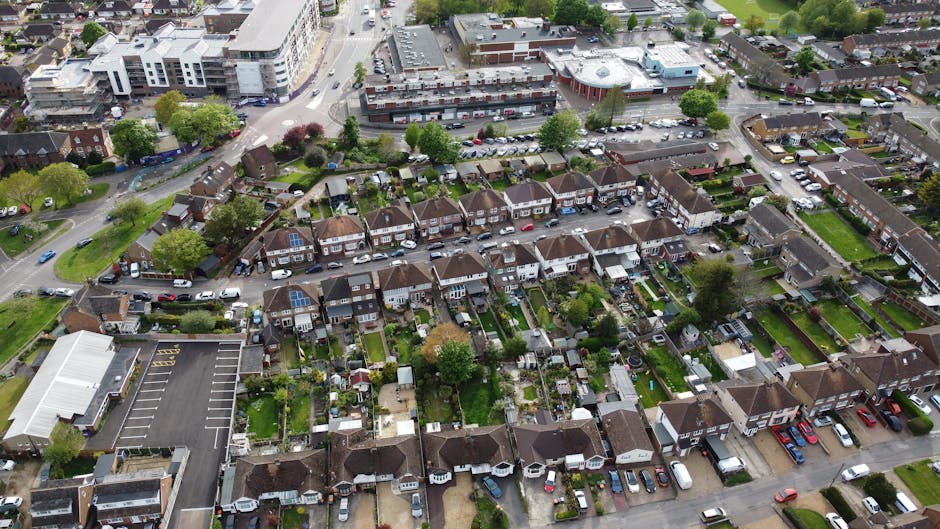 An aerial view of a residential neighbourhood showing a row of terraced and semi-detached houses, many with small, well-maintained gardens, some with solar panels on their roofs. In the foreground, a 