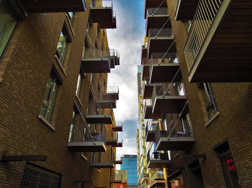 A street scene showing a row of traditional brick commercial and residential buildings with large white-framed windows, some with decorative brickwork, situated along a busy urban road. In front of th